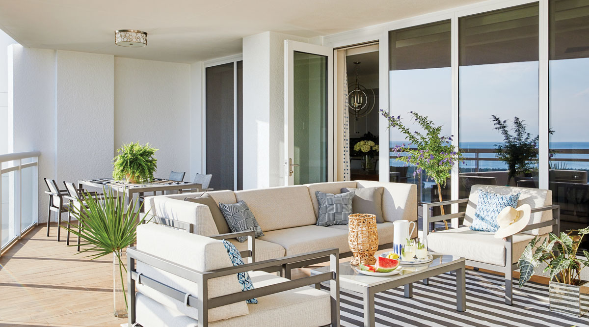 Glass doors open to extend the indoor living spaces out to the balcony. The orchestrated palette echoes the colors and textures found in the sandy beachside landscape. An array of Pavilion furnishings shapes the open-air social spaces anchored by an awning-striped Dash & Albert area rug.