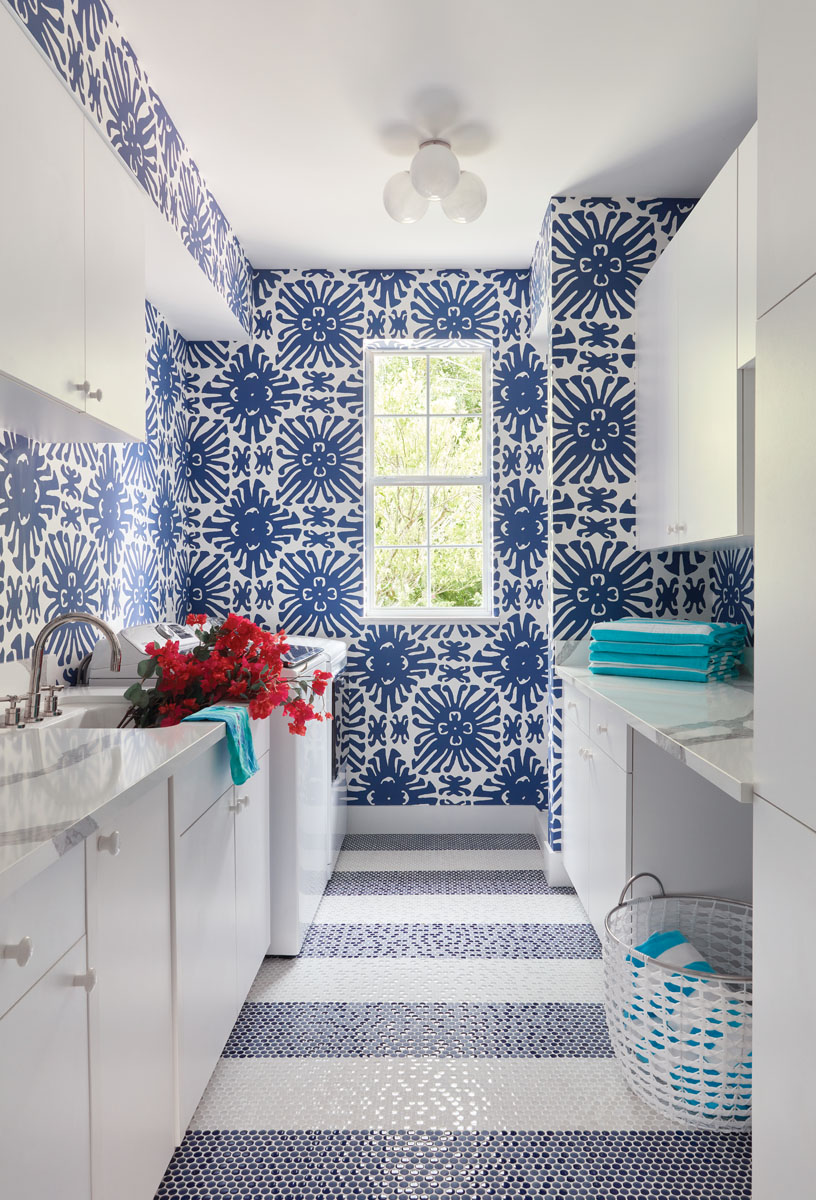 Since the laundry room is the first room you see when entering from the garage, a bold navy and white China Seas wallpaper is paired with a striped, penny-tile floor chosen by George Ross.