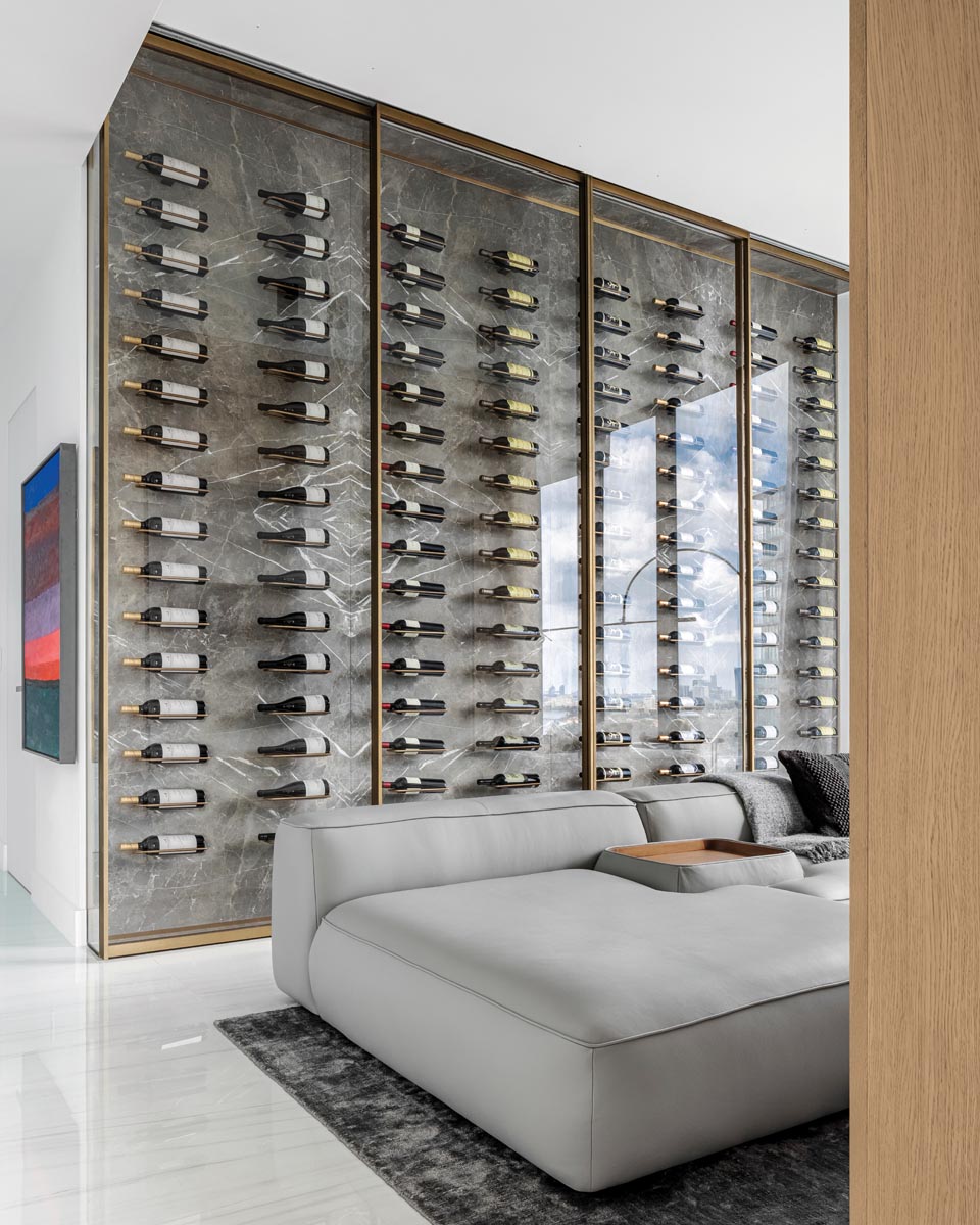 A floor-to-ceiling marble wine wall houses 130 bottles of the husband’s favorite reds, with each bottle cradled in custom, oval brass rings anchored into the marble. A nine-foot-wide gray leather Haute Living sofa fronts the media center.