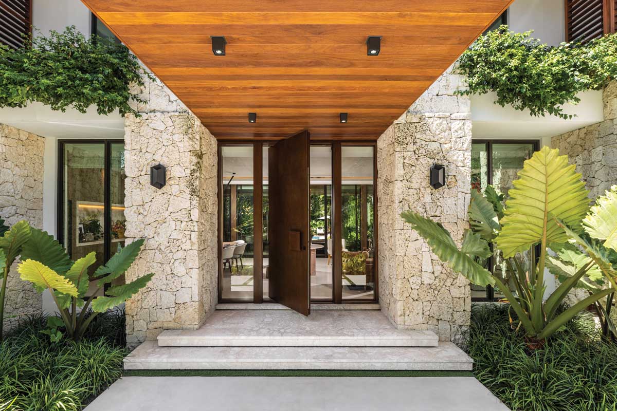 Amplifying the grandeur of the front entrance, massive columns of cut coral stone flank an oversize custom swivel door that makes a dramatic statement. The entry door and ceiling are crafted from two different shades of Brazilian chestnut.