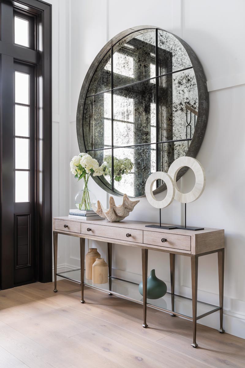 Visitors are welcomed by an elegant entrance foyer and stair tower featuring custom millwork that extends to the second floor. A massive antique mirror reflects natural light, infusing the space with warmth and visual impact.