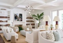 Earth-toned upholstery was chosen for the sofas and chairs in the living room. The custom bookshelves are filled with color-blocked volumes. The duo of lamps is from Paul Schneider Ceramics and the chandelier is from Neirmann Weeks.