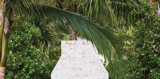 The purposely distressed surface of the custom outdoor fireplace in this backyard vignette from Kemble Interiors is ideal for the backdrop of lush greenery that surrounds it
