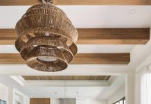 The living room’s soaring height demanded an overscale light fixture with a woven finish that adds to the resort-like ambience. Immediately noticeable are the white oak beams on the ceiling, which bring a sense of warmth to the room. Neutral furnishings below keep the room’s textures balanced.