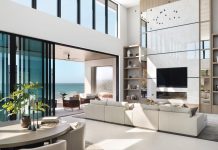 The living room’s massive entertainment wall features porcelain slabs from Atlas Plan, separated by brass strips and flanked by antique mirror panels framed in white oak. A custom rug by Trinity Design anchors the sleek Century sofa, and a Zaneen chandelier illuminates overhead.