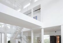 A view into the living room reveals the home’s soaring ceilings and an upper level showcasing a massive painting by Hubert Dziedzic that creates a thoughtful connection between tradition and modern expression. White pendants by Flos balance the scale and proportion between the staircase and the elevator.