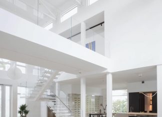 A view into the living room reveals the home’s soaring ceilings and an upper level showcasing a massive painting by Hubert Dziedzic that creates a thoughtful connection between tradition and modern expression. White pendants by Flos balance the scale and proportion between the staircase and the elevator.