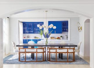 A view of the dining room and kitchen reveals the bold blue cabinetry that the homeowners insisted on at their first meeting with the design team. “It’s a high-gloss lacquer finish, which really makes the blue color pop,” says McCauley. “Since the kitchen is visible from the living room, we knew it would become a focal point.” The centerpiece of the dining area is a light pendant by Gabriel Scott.