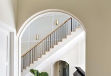 Soaring ceilings and a sweeping staircase highlight the grandeur in this elegant Fort Myers home. The grand piano infuses dramatic contrast into the neutral palette expressed through a pedestal table from CFC and ottomans upholstered in a pale blue Cowtan & Tout fabric.