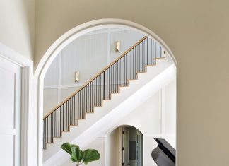 Soaring ceilings and a sweeping staircase highlight the grandeur in this elegant Fort Myers home. The grand piano infuses dramatic contrast into the neutral palette expressed through a pedestal table from CFC and ottomans upholstered in a pale blue Cowtan & Tout fabric.